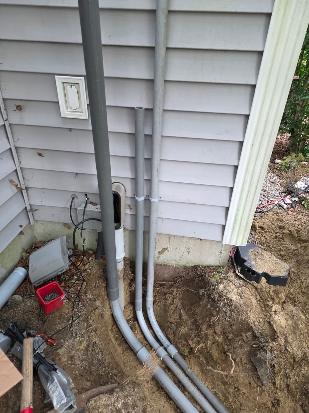 Three PVC conduit runs strapped to the side of a house and swept down into an underground trench