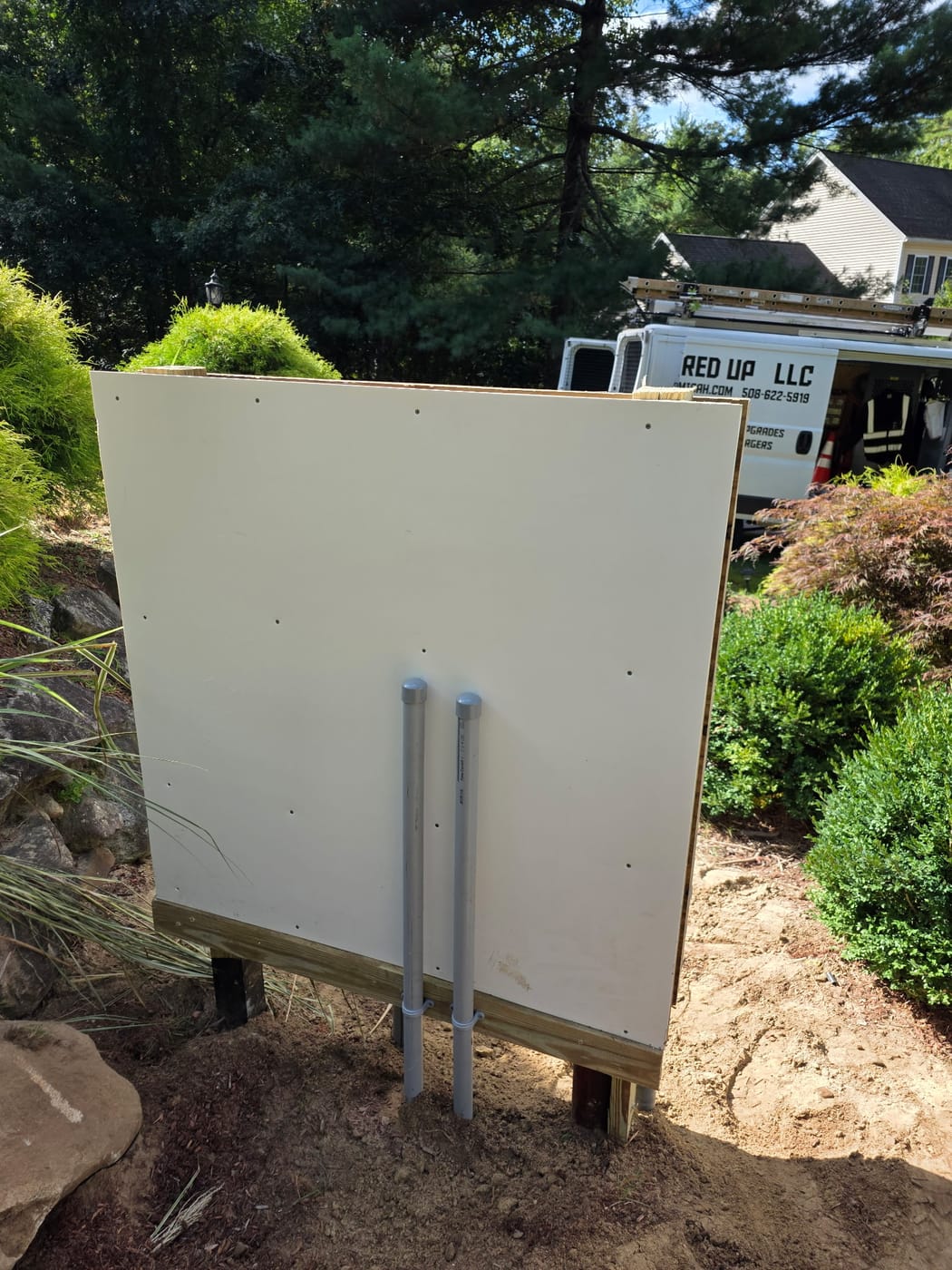 Back of the meter pedestal board with two conduits strapped up, Powered Up LLC van in the driveway