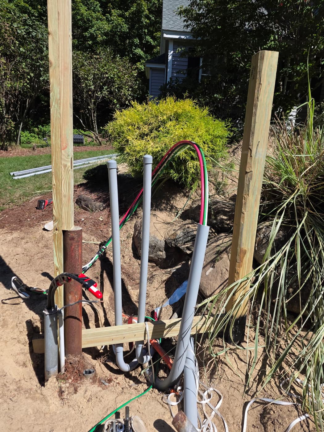 Underground service conduits stubbed up between two pressure-treated posts with feeder conductors pulled through